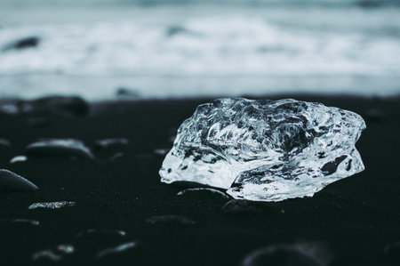 Piece of glacier lying on black sand beach and pebbles agains blue background of Atlantic oceanの写真素材
