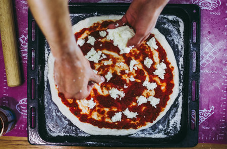 Homemade pizza preparation process. A pizzaiolo covering pizza with mozarella piecesの写真素材