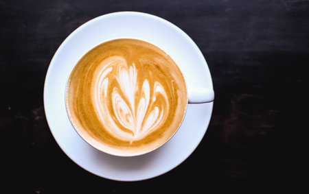White cup of cappuccino with an abstract drawing on a brown coffee foam. Elegant coffee art. Concept background of cafe, rest, leisure, and romantic settings. View from above. Deep black backgroundの写真素材