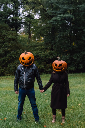 A couple wearing halloween pumpkins on their heads and holding their hands, while standing in an October forestの写真素材