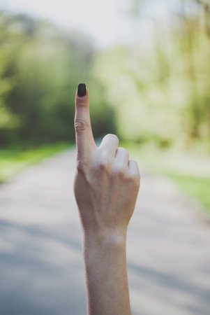 Girl demonstrating a number one (1) gesture against sunny green background.の写真素材