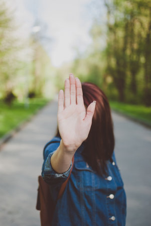 Girl making a stop gesture against sunny green natural background. Open palm