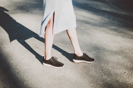 Girl crossing the road and her figure casting deep dark shadow. Sunlight over the asphalt. Pale white women's legsの写真素材