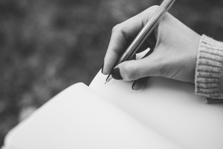 Tender girl's pale hand holding a pen and writing on the blank pages of a notebook. Concept (idea) of dreaming, planning, motivation, studying. Black and whiteの写真素材