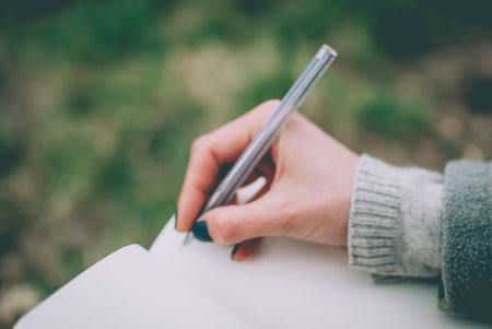 Blurred defocused background. Tender girl's pale hand writing in notebook with blank pages. Concept...