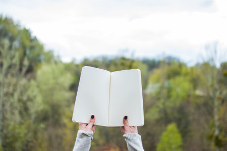 Girl holding a notebook. Pale hands and blank paper of notebook. Concept (idea) of thinking, dreaming, motivation, planning, studying. Backgroundの写真素材
