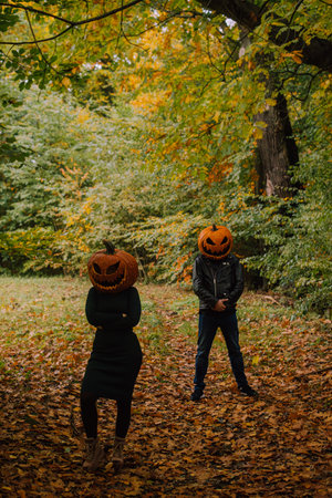 A couple wearing halloween pumpkins standing one behind another in a forest settingの写真素材