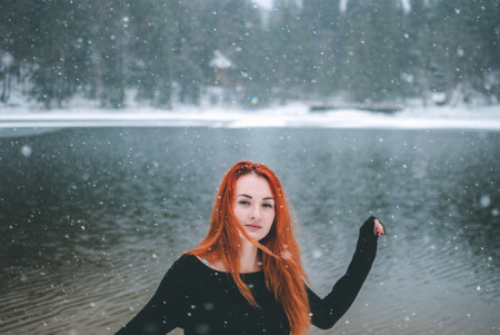 Joyful handsome black-eyed redhead girl looking at the camera. Splendid shady black mountain lake...