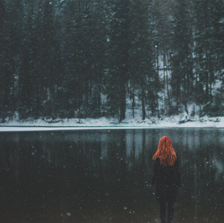 Square-shaped. Snowflakes flying over handsome black-eyed redhead girl looking in the distance. White snowflakes flying all around. Splendid shady black mountain lake. Look from behindの写真素材