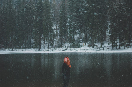 Snowflakes flying over handsome black-eyed redhead girl looking in the distance. Splendid shady...