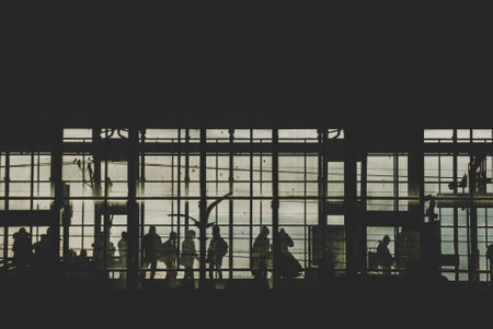 Black sillhouettes of people huttying up to take a train on a subway station behind glass windows filled with sunshine. Berlin, Germanyの写真素材