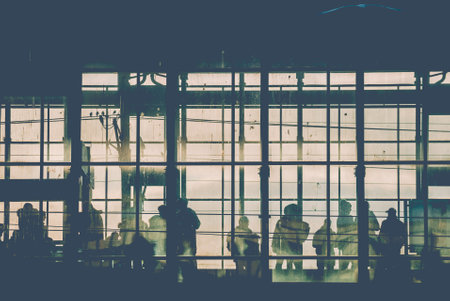 Black sillhouettes of people waiting for their train on a subway station behind glass windows filled with sunshineの写真素材