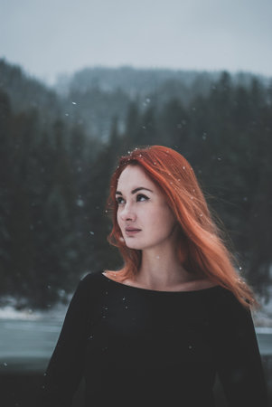Handsome redhead girl looking in the distance. Snowflakes falling on her hair. Splendid shady black...
