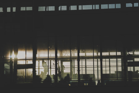 Black sillhouettes of people waiting for their train on a subway station behind glass windows filled with sunshineの写真素材