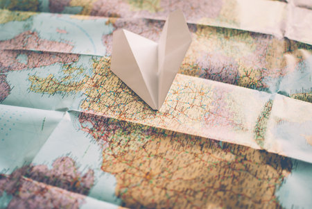 Closeup of a traveler's road map in vintage retro colors. White paper plane flying over Europeの写真素材