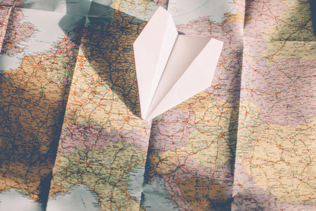 Closeup of a traveler's road map in vintage retro colors. White paper plane flying over Europeの写真素材