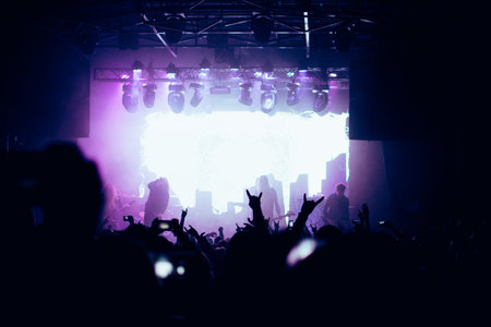 Fans raising their horns up - metal fingers - cheering the band during the show. Hands silhouettes and a band on a stage.の写真素材