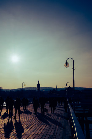 Silhouetted people walking along Sopot pier at sunset with lamps and long shadows.の写真素材