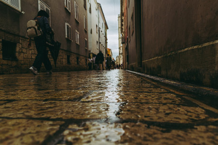 Wet stone street in Zadar, Croatia, after rain, with pedestrians under cloudy skies and a moody atmosphere.の写真素材