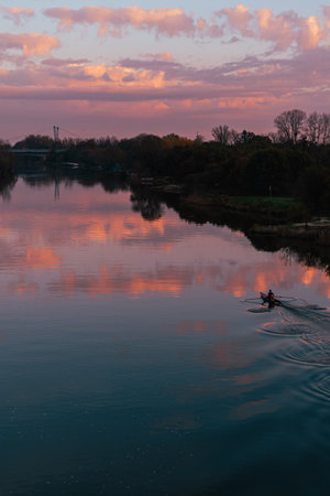 A lone kayaker trains on the Odra River in WrocÅaw during sunset, gliding across the water under pink and orange clouds, creating a nostalgic yet energetic scene.の写真素材