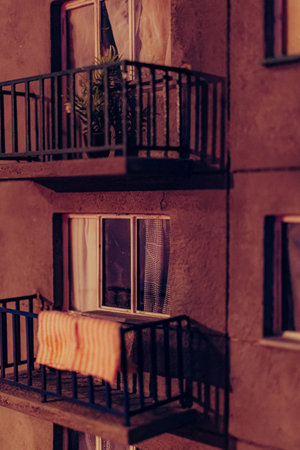 Close-up of a weathered apartment balcony at night, with dim light, curtains, and a striped cloth suggesting everyday domestic life.の写真素材