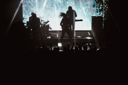 Metal band playing on a stage of a club, cold white and blue light on the screen behind them. People in crowd clapping and going wildの写真素材