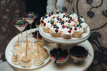 Sweet table. A plates of cakes and muffins with cream with berries. Table with sweets, candy, buffet. Dessert table for a party goodies. Close up. party reception, decorated in restaurant. candy barの写真素材