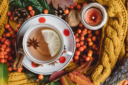 Flat lay of autumn leaves, candles and textured scarf on wooden background with cup of tea. Autumn or Winter concept.の写真素材