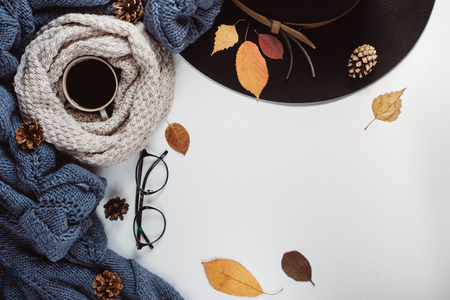 Flat lay-out of the leaves and tartan textured blue sweater on a white background with a cup of coffee, glasses and a hat. Autumn concept.の写真素材