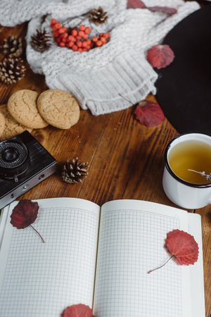 Flat lay-out of autumn leaves and tartan textured sweater on a wooden background with a cup of tea. Autumn or Winter concept.の写真素材
