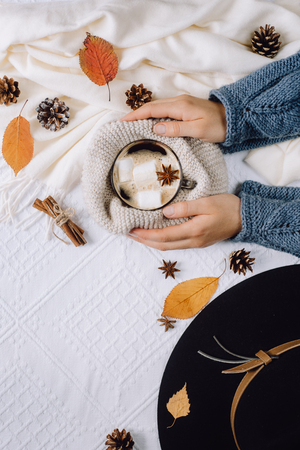 Autumn and Winter composition. Women's hands holding a cup of hot coffee with marshmallows, scarf, cookies, bumps and autumn leaves. Flat lay, top viewの写真素材