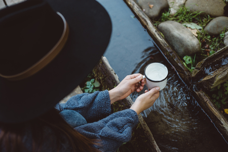 Woman in hat gathers water in a mug from forest on time hiking trip. Concept adventure active vacations outdoor. Campingの写真素材