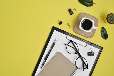 Office desk workspace with blank clip board, office supplies, pen, cactus, green leaf, coffee cup...