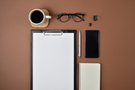 Mockup workspace with blank clip board, office supplies, pen, notepad, smartphone, coffee cup and...
