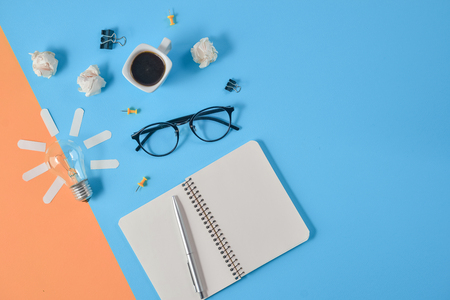 Flat lay financial planning brainstorming messy table top image with blank clip board, office supplies, pen, notepad, eyeglasses, coffee cup, light bulb on orange and blue background.の写真素材
