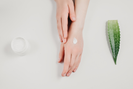 Beautiful groomed woman's hands with organic cream jar and Aloe vera fresh leaves on white background. Moisturizing cream for clean and soft skin. Flat lay, top view, copy space. Healthcare concept.の写真素材