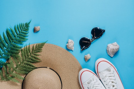 Traveler accessories, tropical fern leaf branches, hat, sunglasses, footwear and seashell on blue background. Travel vacation concept. Summer background. Flat lay, top view, copy spaceの写真素材