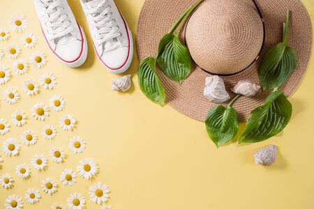 Flat lay traveler accessories on yellow background with green leaf, hat, footwear, seashell and...