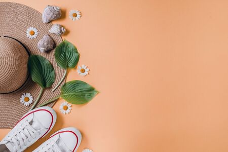 Traveler accessories, tropical leaf, hat, footwear and seashell on orange background. Travel...