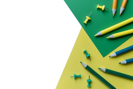 Creative flat lay back to school concept with colored pencils and office supplies on white, green and yellow background. Flat lay, top view, copy space.の写真素材