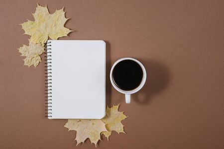 Workspace with golden maple leaves, bumps, notebook and cup of coffe on brown background. Creative composition. Autumn or Winter concept. Flat lay, top viewの写真素材