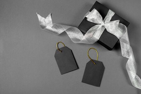 Black friday sale concept. Black paper boxes with silver ribbon, price tags on gray background. Flat lay, top view, copy spaceの写真素材