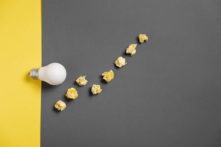 New idea concept with crumpled office paper and white light bulb on black and yellow background. creative solution during brainstorming session. Flat lay, top view, copy spaceの写真素材