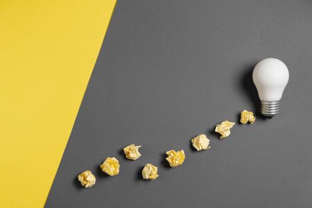 Creativity inspiration, great business idea concept with white light bulb and paper crumpled ball on gray and yellow background. Flat lay, top view, copy spaceの写真素材