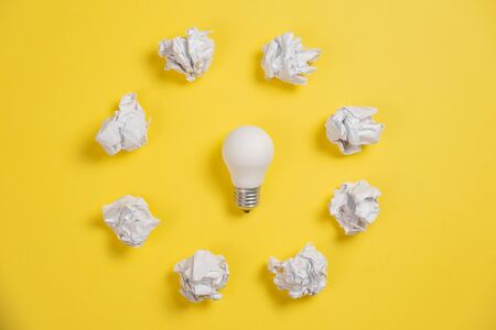 new idea concept with crumpled office paper and white light bulb on yellow background. Creative solution during brainstorming session concept. Flat lay, top view, copy spaceの写真素材