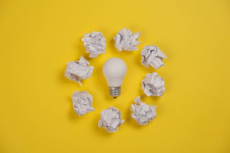 Creativity inspiration, great business idea concept with white light bulb and paper crumpled ball on yellow background. Flat lay, top view, copy spaceの写真素材