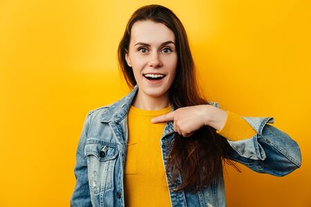 Portrait of attractive beautiful young woman points hand at herself, can not believe her luck, has...