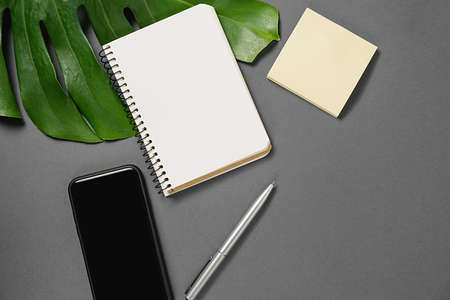 Creative top view flat lay of desk with pen, tropical monstera leaves, notebook, modern smartphone with copy space on gray paper background minimal style. Template for blog social mediaの写真素材