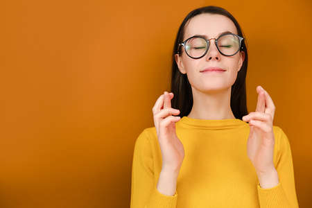 Beautiful young female in glasses model dressed sweater, keeps fingers crossed, waits for special...