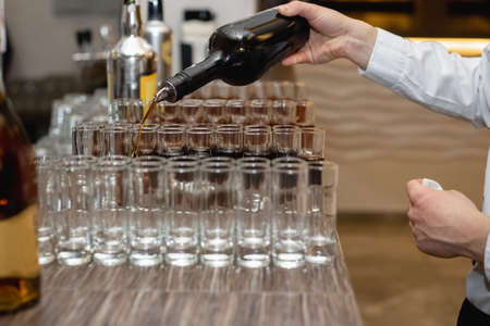 Close up of bartender pours alcoholic drink into small glasses on bar. Party and holiday celebration...